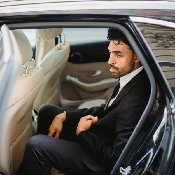 A bearded man in a black suit sits elegantly inside a luxury car, exuding sophistication.